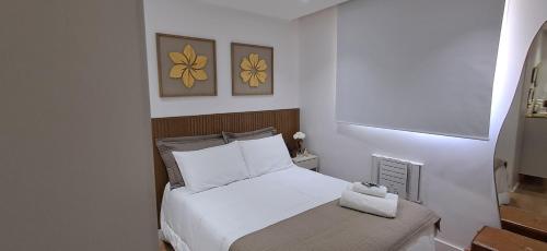 een slaapkamer met een wit bed en twee foto's aan de muur bij Riocentro, Projac, Parque Olímpico, apartamento completo com vaga! in Rio de Janeiro