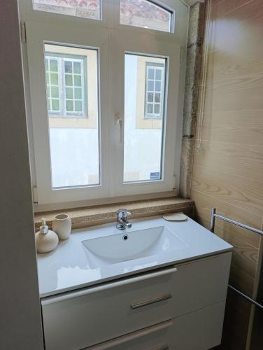 a bathroom with a white sink and two windows at Casa do Pelourinho in Coja