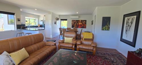 a living room with a couch and chairs and a kitchen at Bumble Bee Cottage in Kerikeri