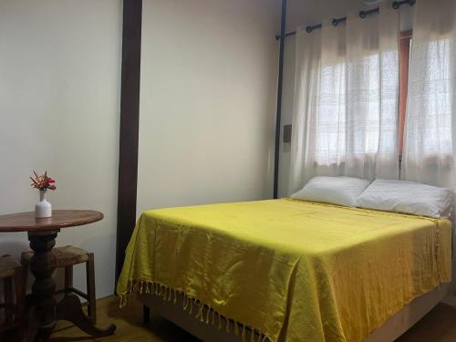a bedroom with a bed with a yellow bedspread and a table at Suíte da Alê in Marau