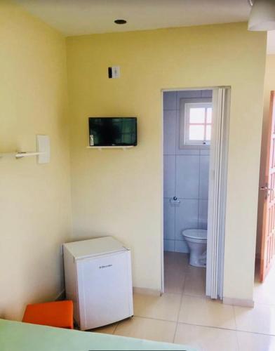 a bathroom with a toilet and a television on the wall at Porto Pousada com café in Imbituba