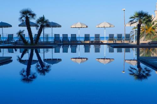 a pool of water with chairs and umbrellas at Aparthotel Caprice Skyline in Ciutadella