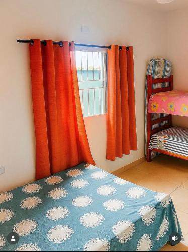 a bedroom with orange curtains and a bed and a window at Palace Massaguaçu in Caraguatatuba