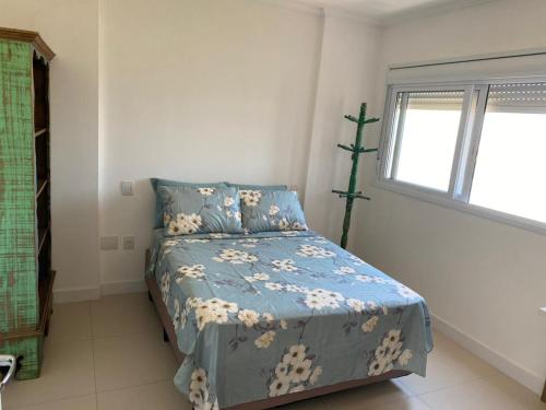 a bedroom with a bed with a blue comforter and a window at Apê da Paula in Torres
