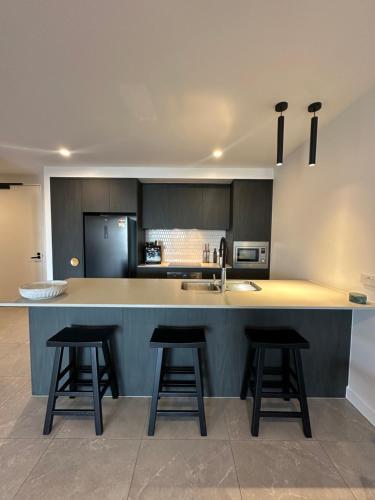 une cuisine avec trois tabourets de bar et un comptoir dans l'établissement Avalon Maroochydore, à Maroochydore