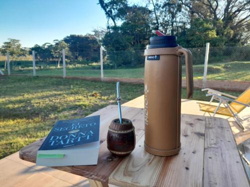 a thermos on a wooden table with a book and a drink at Cabaña Alpina Zen in Carmen del Paraná