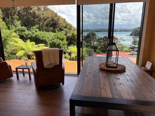 a living room with a wooden table and a view of the ocean at Tuis Nest, family beach bach at Opito Bay in Kerikeri