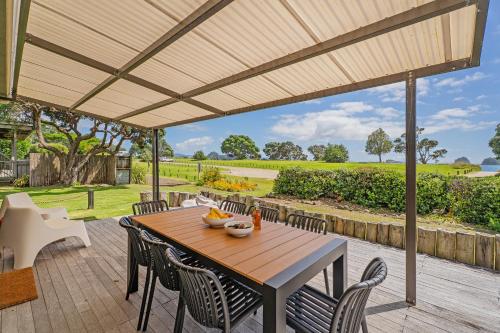 Hosts on the Coast Hahei Sands Villa B في هاهي: طاولة وكراسي خشبية على الفناء