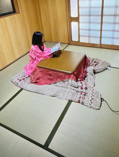 a girl sitting on a blanket reading a book on a table at ゲストハウス輪 高野山麓 in Hashimoto