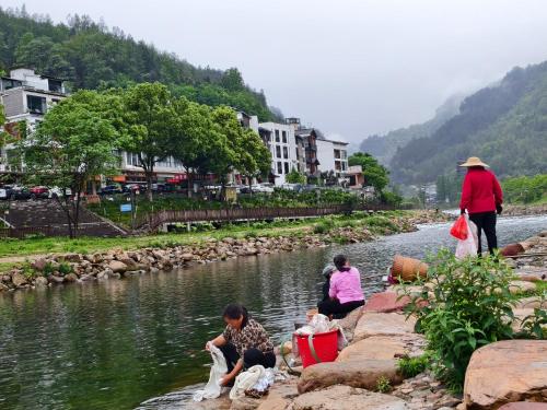 a group of people sitting on the side of a river at 张家界武陵源山边溪上客栈-About a 10-minute walk from the east gate of the Forest Park - there is a beautiful little river at the entrance - free recommended travel routes provided - Tickets for attractions can be booked in advance in Zhangjiajie