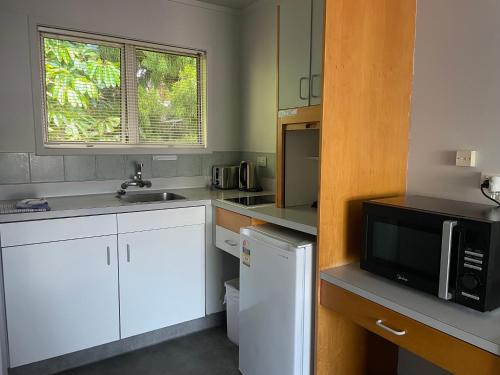 a kitchen with white cabinets and a microwave at Aaron Court Motel Whangarei in Whangarei