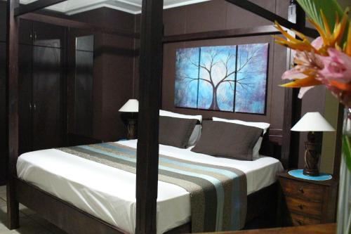 a bedroom with a bed with a tree painting on the wall at Stephna Residence in Anse Boileau