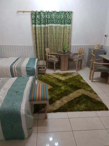 a room with two beds and a table and a rug at Hill View Hotel West Airport in Accra