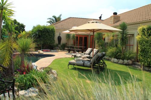 a garden with a couch and an umbrella next to a pool at Villa Chad Luxury Guesthouse in Kleinmond