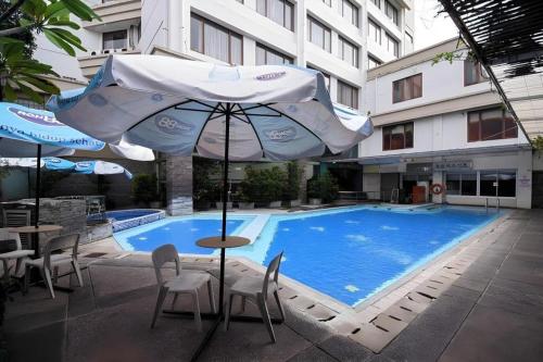 Una piscina con sombrilla y sillas y una mesa con mesa. en Kedaton Hotel, en Bandung