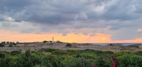 a sunset with a lighthouse on a hill with trees at Phaedrus Living Venus Seaview Lighthouse Villa in Paphos