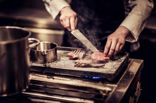 a person cooking meat on a grill with a knife at Carlton Square Hotel in Haarlem