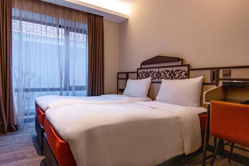 two beds in a hotel room with a window at Aqueen Prestige Hotel Lavender in Singapore
