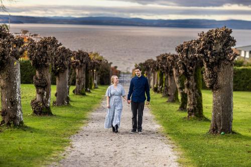 a couple walking down a path with the ocean in the background at Hotel Refsnes Gods - by Classic Norway Hotels in Moss