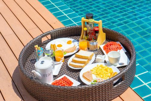 パナワビーチにあるPhuket Boat Quay Hotel Panwa Beachのプールの横に朝食の食べ物と飲み物が詰まったバスケット