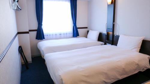 two beds in a hotel room with a window at Toyoko Inn Shin-osaka Higashi-mikuni Ekimae in Osaka