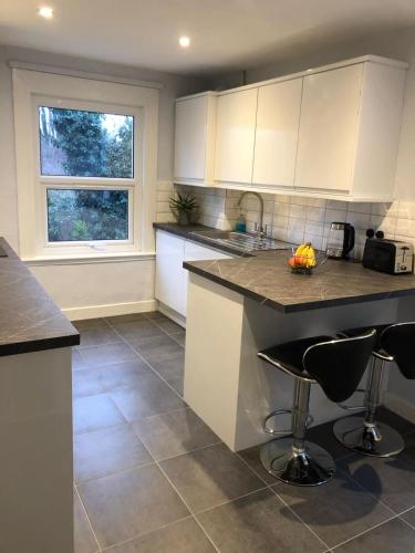 a kitchen with white cabinets and a counter with bar stools at 1 bedroom flat 15 minutes from Oxford Circus in London