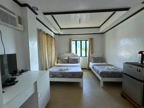 a room with two beds and a desk and a television at Florabells Guest House - Batanes in Basco
