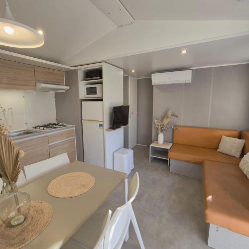 L'Oasis Mobil Home à 100m de la Plage Camping 5 étoiles في توراي: مطبخ وغرفة معيشة مع طاولة وأريكة