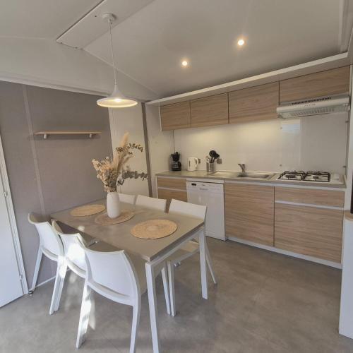 L'Oasis Mobil Home à 100m de la Plage Camping 5 étoiles في توراي: مطبخ مع طاولة بيضاء وكراسي بيضاء