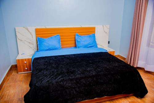 a bed with a black blanket and blue pillows at Happy Home House in Ruhengeri