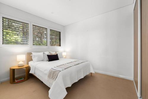 ein weißes Schlafzimmer mit einem Bett und zwei Fenstern in der Unterkunft Upper North Shore Haven - A Tranquil Treetop Escape in Warrawee