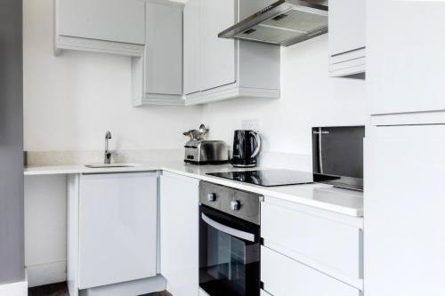 a white kitchen with white cabinets and appliances at The Regency | Seafront Lux Apartments! in Southend-on-Sea