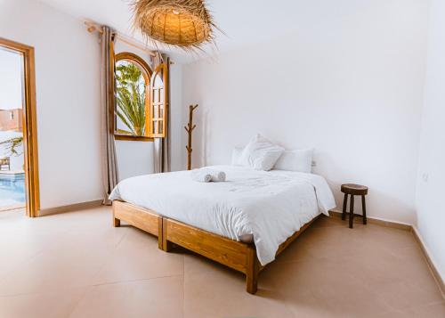 a bedroom with a bed with white sheets and a window at Riad TAWALA Surfing Mind in Tamraght Ouzdar