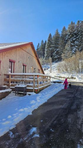 Een persoon in een roze jas knielt in de sneeuw naast een gebouw. bij La Ferme du Badon in Gérardmer