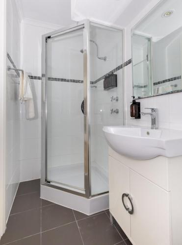 a white bathroom with a shower and a sink at Coastal Views - waterfront guest apartment in Daleys Point