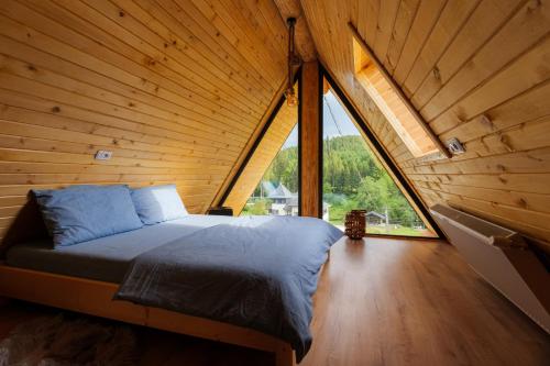 a bed in a wooden room with a large window at Chilia Houses in Mănăstirea Humorului