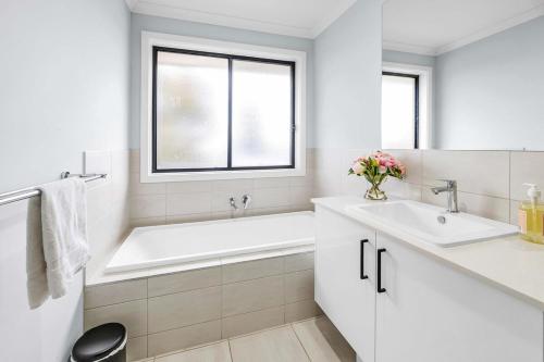 a white bathroom with a tub and a sink at Bright & Cozy 4-Bed Home in Rockbank in Rockbank
