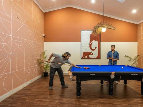 two men playing pool in a room with a pool table at The Hosteller Bam Coorg in Madikeri
