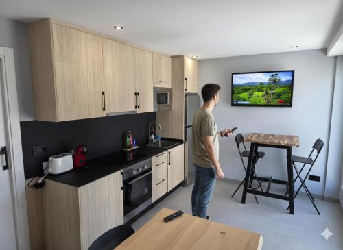 a man standing in a kitchen with a tv on the wall at Apartamentos Camino Inglés II in Ordes