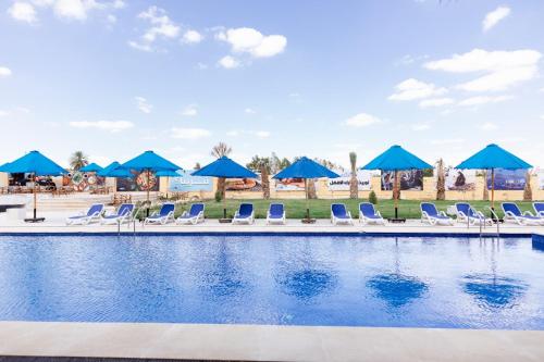 a pool with lounge chairs and blue umbrellas at فندق لوريت in Qaryat at Ta‘mīr as Siyāḩīyah