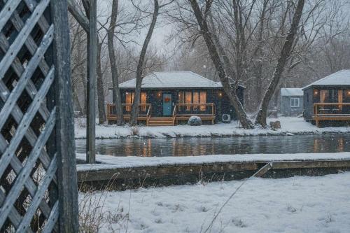 2-bedroom Lake Front Cottage in Harwood ON #4 في Harwood: كابينة خشب في الثلج بجانب النهر