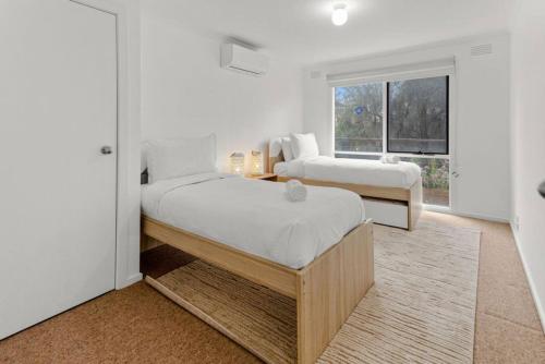 a white bedroom with two beds and a window at Saltwater Shack in Anglesea