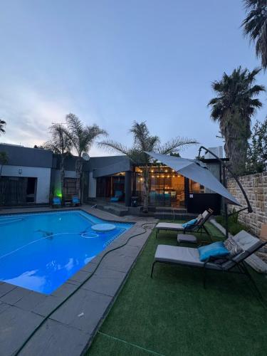 a swimming pool with two lounge chairs and a house at Zee Lifestyle Guesthouse in Vanderbijlpark