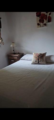 a white bed with a pillow and a night stand at Cabañas en monte autóctono con pileta in San Marcos Sierras