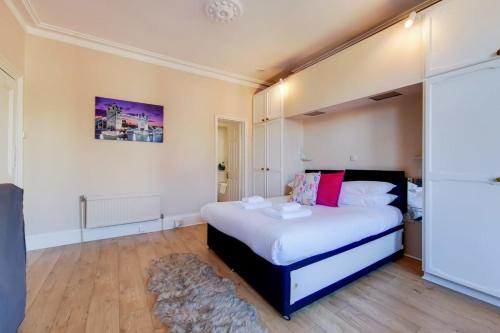a bedroom with a bed with white sheets and pink pillows at Comfortable Ealing Apartment with Workspace in London