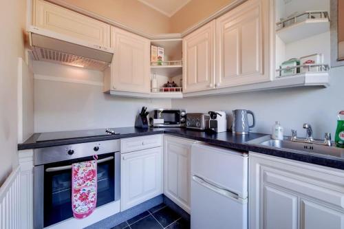 a kitchen with white cabinets and black counter tops at Comfortable Ealing Apartment with Workspace in London
