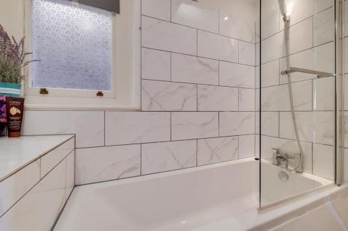 a white bathroom with a tub and a window at Comfortable Ealing Apartment with Workspace in London
