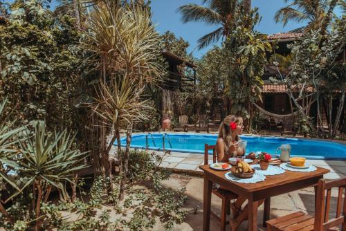 a woman sitting at a table in front of a pool at Pousada Fortal Jeri in Jericoacoara