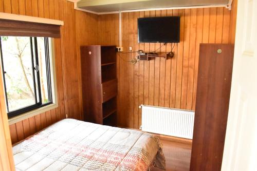 Habitación pequeña con cama y TV en la pared. en Cabañas Mister Nelson, en Valdivia