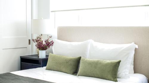 a white bed with white pillows and a vase of flowers on a table at ONeill I by AvantStay Coastal Paradise Steps from Beach Modern Decor in Newport Beach